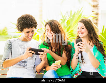 USA, Jupiter, en Floride, Groupe d'amis (14-15) assis sur un banc et texting Banque D'Images