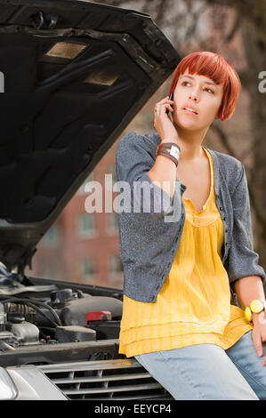 Woman on cell phone s'appuyant sur la voiture avec le capot ouvert Banque D'Images