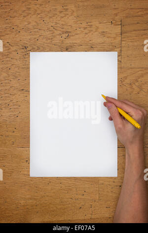 Hand holding pen sur une feuille de papier blanc sur une surface de table en bois usé, vu du dessus Banque D'Images