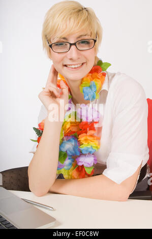 Blonde woman sitting at desk et portant un lei Banque D'Images