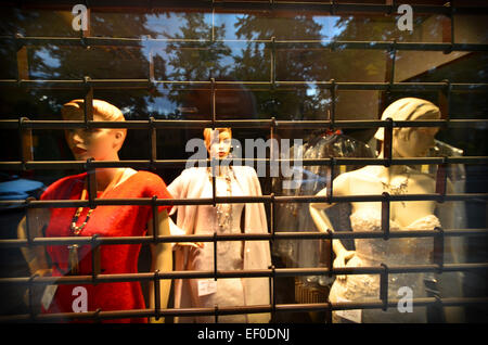 Des mannequins dans une vitrine au regard de nuit à travers la grille de sécurité avec la réflexion de le ciel du soir dans la fenêtre, Banque D'Images