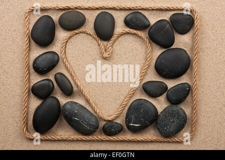 Beau cadre de corde dans la forme de coeur avec les pierres noires, sur le sable Banque D'Images