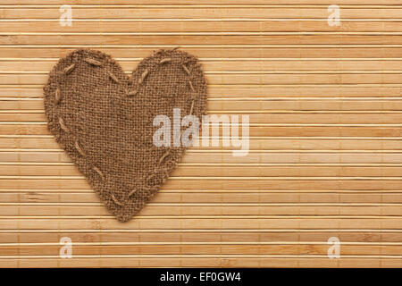 Le cœur symbolique de la toile de jute se trouve sur un tapis de bambou, comme un arrière-plan Banque D'Images