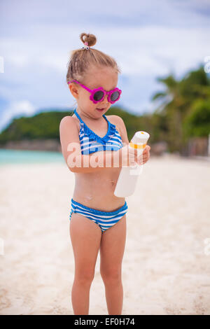 Peu cute adorable fille en maillot de bain se frotte elle-même d'un écran solaire Banque D'Images