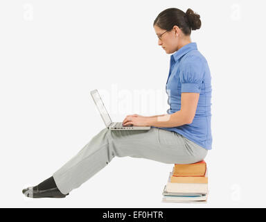 Woman typing on laptop, assis sur une pile de livres Banque D'Images