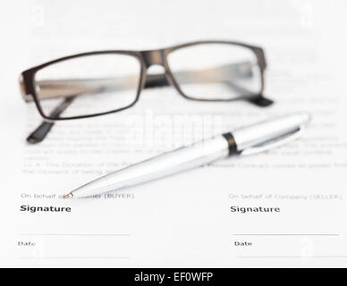 Plume d'argent et les lunettes sur la page de signature du contrat de vente Banque D'Images