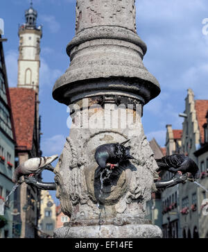 Trois pigeons assoiffés se rafraîchir simultanément à robinets sur une ancienne fontaine de l'eau le long d'une des rues principales de la ville médiévale de Rothenburg od der Tauber dans la région de Bavière en Allemagne. Banque D'Images