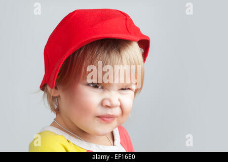 Studio portrait de funny smiling baby girl in red baseball cap sur fond de mur gris Banque D'Images