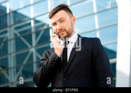 Businessman having conversation with cellphone sur l'arrière-plan bâtiment contemporain Banque D'Images