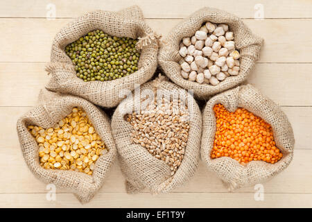 Sacs de jute avec des céréales : lentilles, pois, pois chiches, blé et vert mung sur table en bois, vue du dessus Banque D'Images