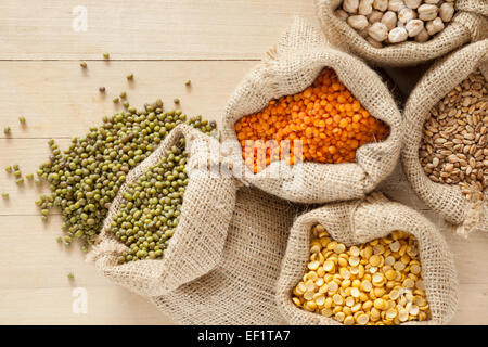 Avec des sacs de céréales : les lentilles rouges, pois, pois chiches, blé et vert mung sur table en bois Banque D'Images