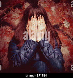 Adolescentes avec les mains au-dessus des yeux près de mur rouge spectaculaire en plein air Banque D'Images