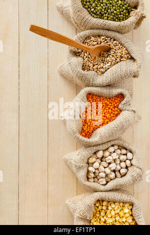 Sacs de jute avec les pois, pois chiches, lentilles, blé et vert mung sur table, vue d'en haut Banque D'Images