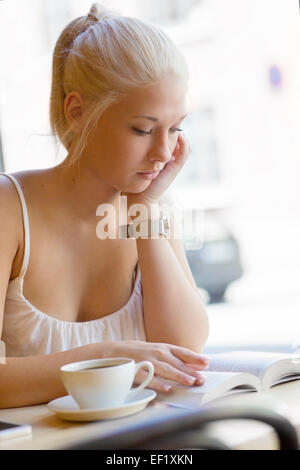 Attractive young woman reads book at cafe Banque D'Images