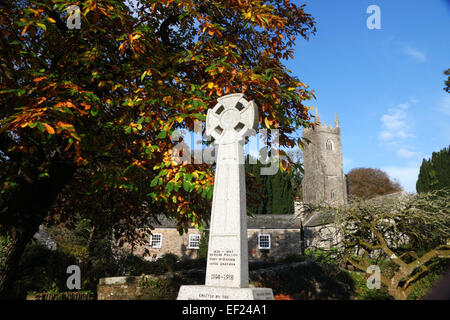 Une croix celtique war memorial sous un arbre à feuillage de l'automne et une église tour derrière. Banque D'Images