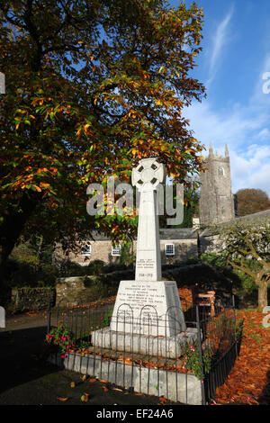 Une croix celtique war memorial sous un arbre à feuillage de l'automne et une église tour derrière. Banque D'Images