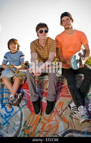 Trois jeunes hommes assis sur un mur à un skatepark Banque D'Images