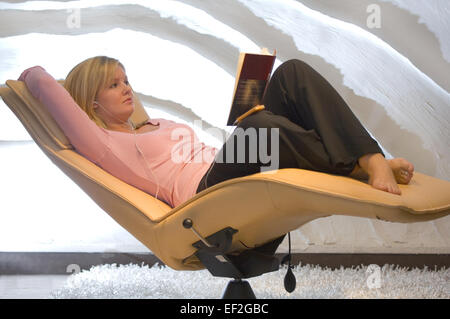 Femme dans un fauteuil moderne à l'écoute stéréo personnelle et la lecture d'un livre Banque D'Images