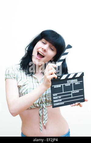 Smiling brunette girl dress up montrant clapper sur fond blanc Banque D'Images