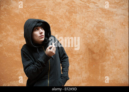 Jeune femme sombre triste et permanent de fumer près de la paroi urbaine portrait Banque D'Images