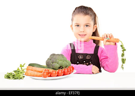 Girl eating un tas de légumes assis sur table isolé sur fond blanc Banque D'Images