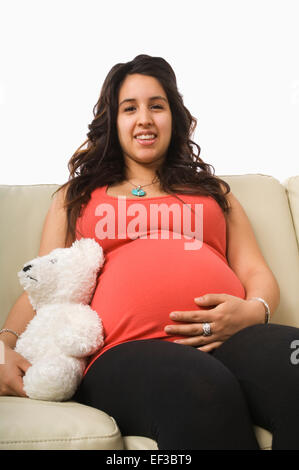 Pregnant woman sitting on couch with teddy bear Banque D'Images