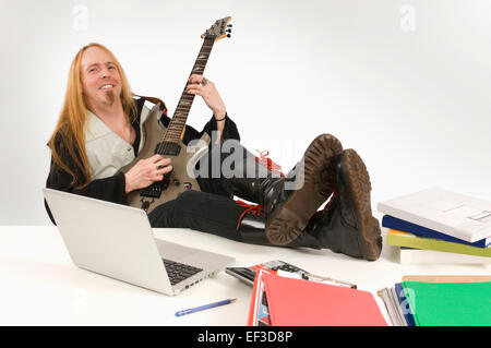 Le guitariste aux cheveux longs sitting at desk Banque D'Images