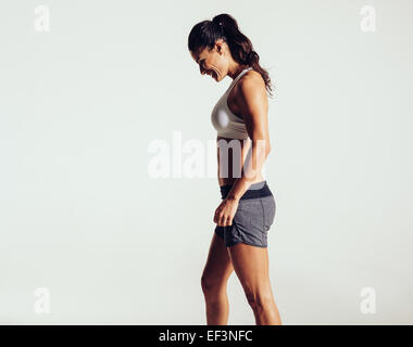 Vue latérale d'happy young woman in sports wear contre fond gris. Femme en riant de remise en forme. Banque D'Images