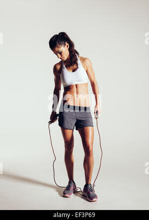 Portrait de l'ajustement et la femme avec la corde à sauter debout sur fond gris. Sports et fitness concept. Banque D'Images