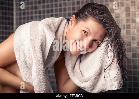 Femme souriante avec les cheveux mouillés dans une douche avec carreaux de mosaïque gris s'essuyant sur une serviette blanche propre Banque D'Images