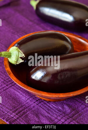 Poisson frais entier aubergines dans un bol en bois sur une serviette mauve Banque D'Images