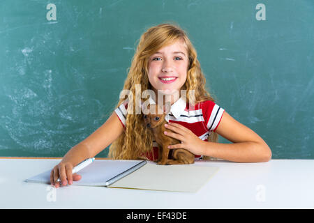 Fille étudiante blonde avec petit chien au bord de la craie verte classe assis dans 24 Banque D'Images