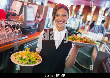 Jolie barmaid holding de salades plaques Banque D'Images