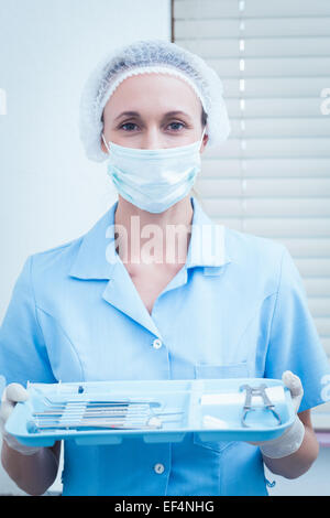 Femme dentiste dans un masque chirurgical holding tray of tools Banque D'Images