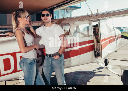 Jeune couple standing by propeller aeroplane Banque D'Images