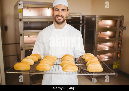Baker smiling at camera holding rack de rouleaux Banque D'Images