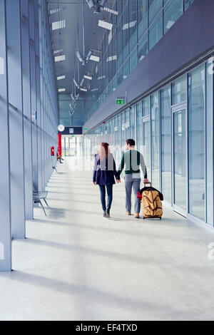 Jeune couple en train de marcher les mains dans les mains à travers la construction de l'aéroport Banque D'Images