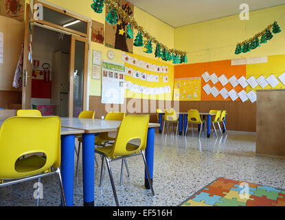 Classe de maternelle avec des chaises et une table jaune avec des dessins d'enfants aux murs Banque D'Images