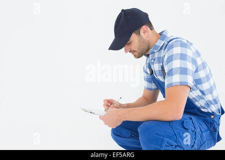 Handyman crouching lors de l'écriture sur le presse-papiers Banque D'Images