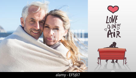 Image composite de smiling couple enveloppé dans la couverture sur la plage Banque D'Images