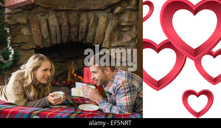 Image composite de couple avec verres en face d'une cheminée allumée Banque D'Images