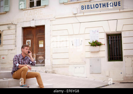 Jeune homme en vacances assis par la mairie de la ville de La Colle sur Loup dans le sud de la France en utilisant son smartphone Banque D'Images