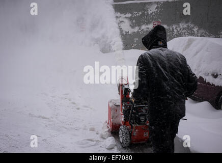 Un homme utilise une souffleuse à neige pour dégager la neige sur un parking lors d'une tempête de neige dans le centre-ville de Boston. Banque D'Images