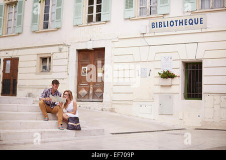 Jeune couple en vacances assis par la mairie de la ville de La Colle sur Loup dans le sud de la France à la recherche sur une carte Banque D'Images