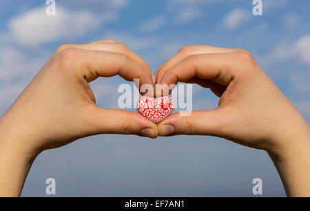 Deux femmes sont titulaires d'un coeur en céramique mouchetée rouge vif contre le ciel bleu avec des nuages. Banque D'Images