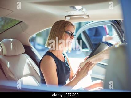 Businesswoman using digital tablet in back seat of car Banque D'Images