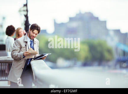 Businessman reading newspaper on urban waterfront Banque D'Images