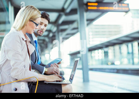 Business people using laptop at train station Banque D'Images