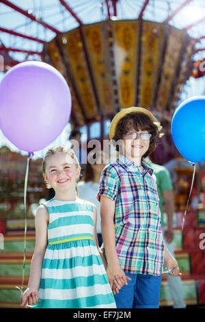 Portrait of boy and girl holding balloons dans amusement park Banque D'Images