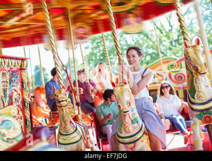 Femme assise sur le cheval de carrousel en amusement park Banque D'Images